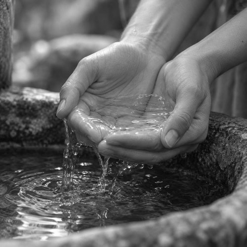 Hände mit Wasser an einem Brunnen
